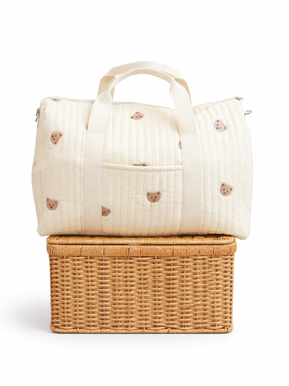 白背景のスタジオで撮影された、くま柄のキルティングボストンバッグ（生成り色）。キャンバス持ち手と前面ポケット付きで、ラタンの収納ボックスの上に置かれている。
