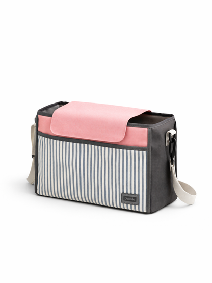 白背景のスタジオで撮影された、ストライプ柄フロントポケット付きのベビー用おむつバッグ。グレーの本体にピンクのフラップ、ショルダーストラップが付いている。
