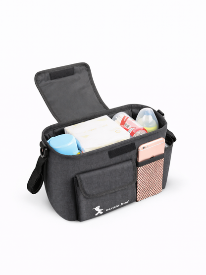 白背景のスタジオで撮影された、フタ付きのグレーのベビーカー用収納バッグ。内側におしりふき・哺乳瓶・小物を入れ、前面ポケットとメッシュポケットにスマホを収納している。
