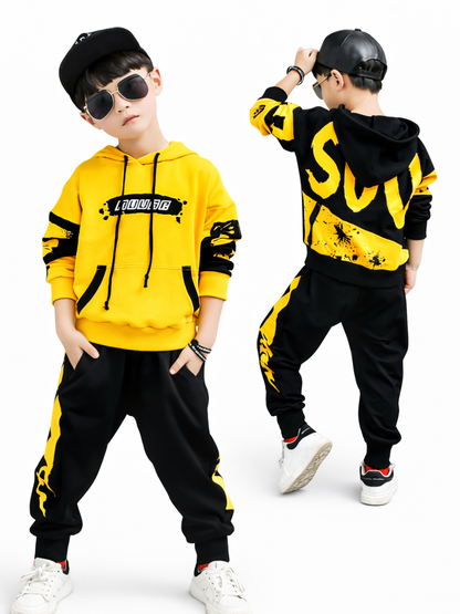 白背景で、黄×黒のストリート系セットアップ（フーディー＋ジョガーパンツ）を着た男の子2ポーズを並べた商品画像。左は正面、右は背面でロゴ柄と配色デザインが分かる。