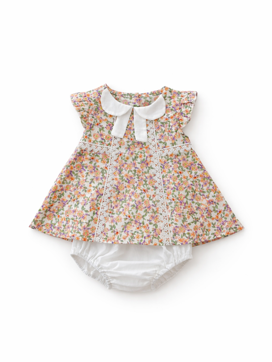 白背景に、小花柄プリントのベビーワンピース（白い襟リボン付き・レース装飾入り）と白いブルマがセットで配置された商品画像。
