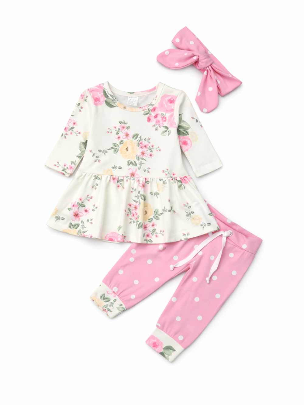 白背景に、花柄プリントのアイボリー長袖ペプラムトップス、ピンクの水玉パンツ（ウエスト紐付き）、ピンク水玉のリボンヘアバンドがセットで配置された商品画像。

