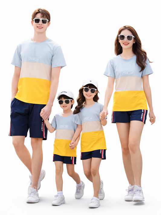 家族4人（両親と子ども2人）が、おそろいの水色×ベージュ×イエローのカラーブロックTシャツとネイビーのショートパンツ、白い帽子とサングラスを身に着け、白背景のスタジオで手をつないで並んでいる。
