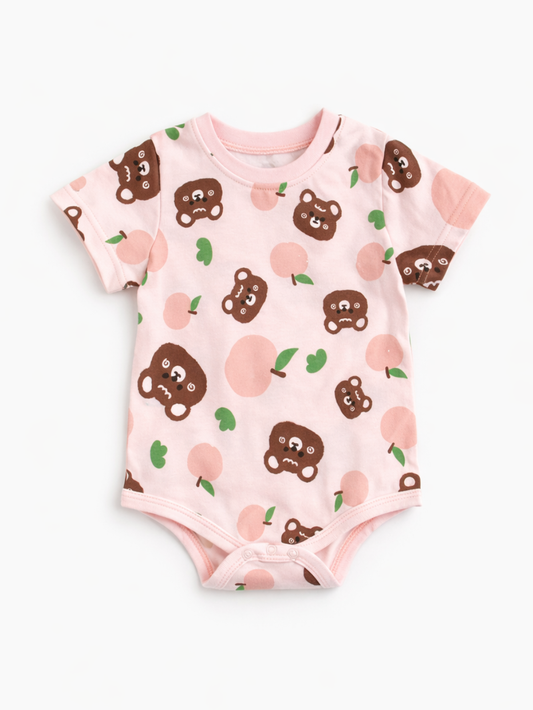 淡いピンク地にくまの顔と桃モチーフの総柄が入った、半袖ベビー用ボディスーツ（ロンパース）。丸首リブ、股下スナップボタン付きで、白背景に平置きで写っている。
