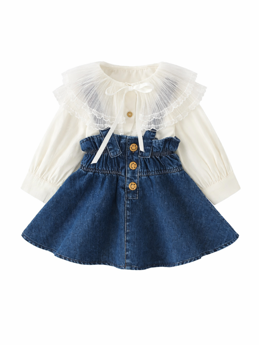 白いシフォン長袖ブラウス（大きなチュール襟・リボン付き）と、スマイルボタンが並ぶハイウエストのデニムスカートを組み合わせた女の子用セットアップの平置き商品画像（白背景）。
