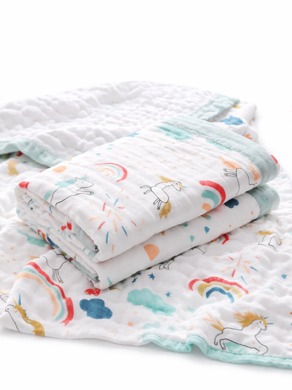 乳児用のガーゼブランケット2枚（ユニコーン・虹・雲のプリント）。1枚はきれいに折りたたまれて上に重ねられ、白いスタジオ背景で柔らかな均一照明、質感がはっきり見える高解像度の物撮り。
