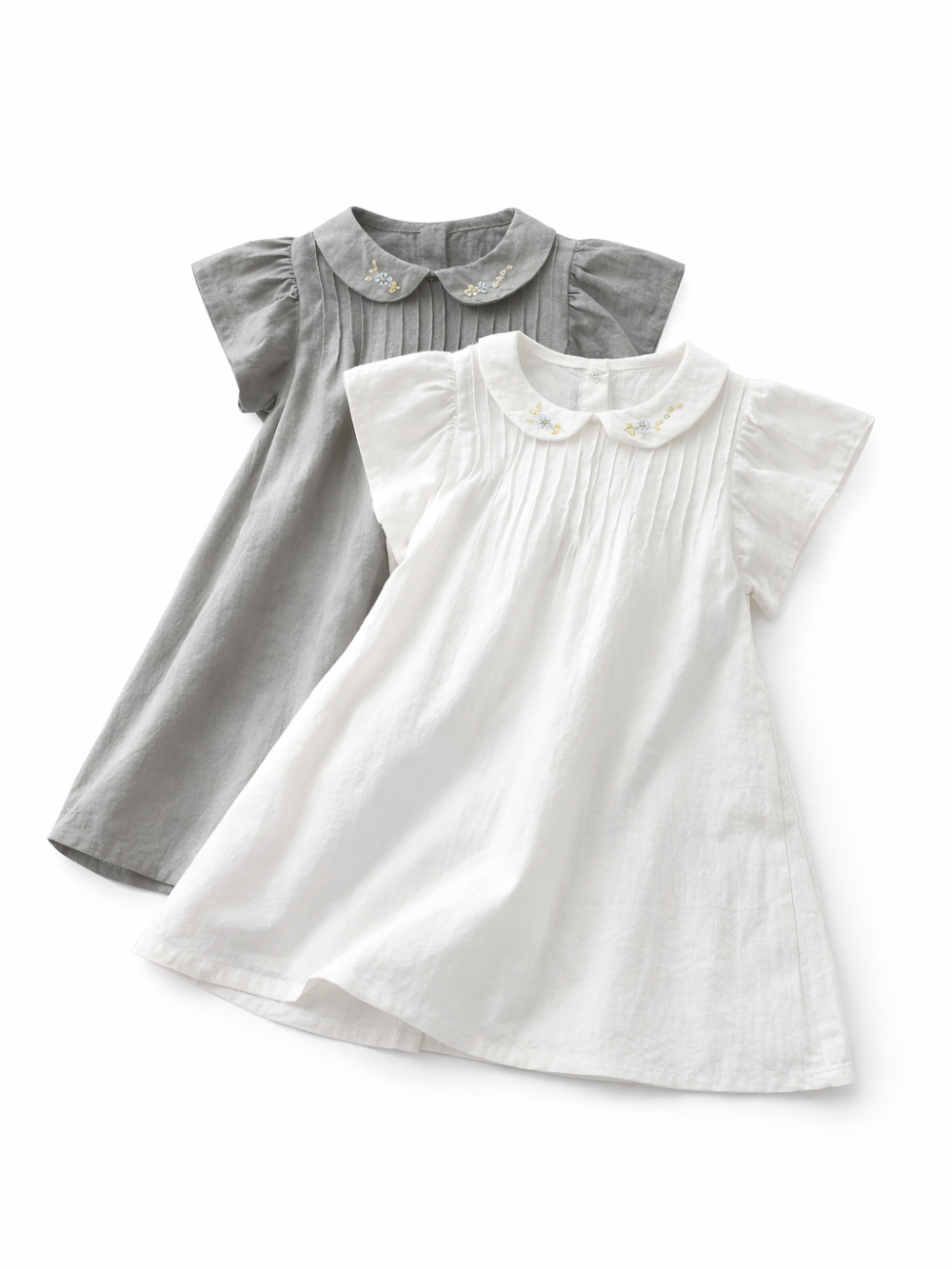 白い背景に、刺繍入りの襟とプリーツのある白いワンピースとグレーのワンピースが重ねて平置きされた商品写真。
