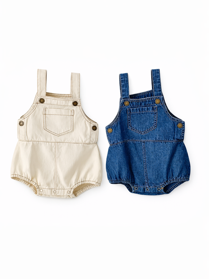 白背景に並んだベビー用デニムサロペットロンパース2点（左：アイボリー、右：ブルーデニム）。肩ストラップとフロントポケット、真鍮風ボタン付きで、ハンガーに掛けて撮影されている。
