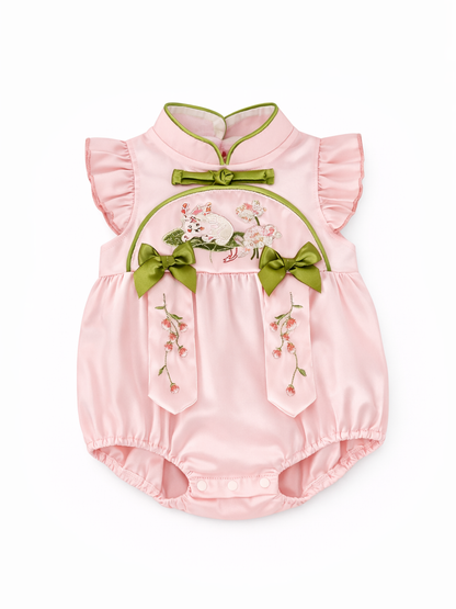 淡いピンクのサテン風ベビーロンパース。グリーンの縁取りを施したチャイナカラーとリボン、うさぎと花の刺繍、花柄の刺繍モチーフがあしらわれ、白い背景に単体で配置されている。
