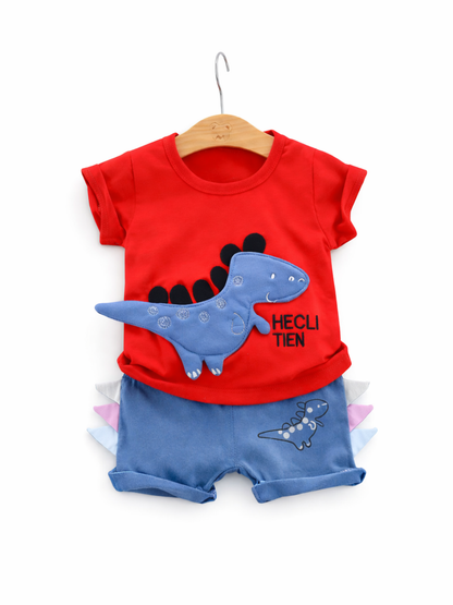 白背景で、木製ハンガーに掛けた赤い半袖Tシャツ（青い恐竜の立体アップリケ付き）と、ブルーのショートパンツ（サイドにカラフルな三角スパイク装飾・恐竜プリント）を組み合わせた子ども用上下セットの商品画像。
