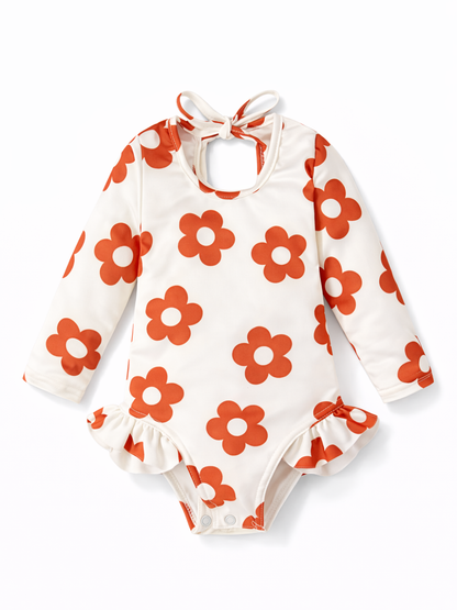 ベージュ地にオレンジの花柄が入った、長袖のベビー用ロンパース（首元リボン付き）を白背景で撮影した商品画像。
