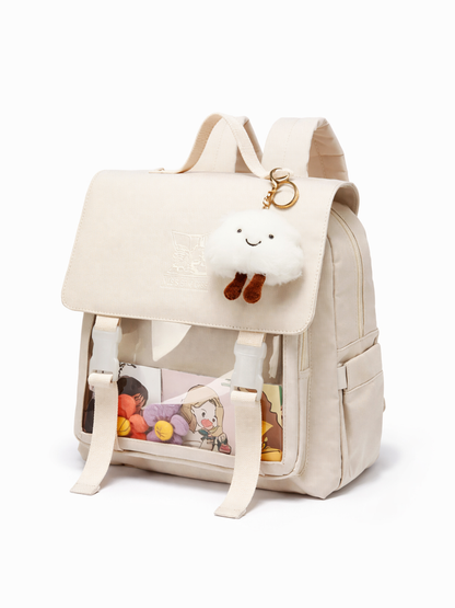 生成りカラーのキャンバス風リュック。フラップ留めベルトと透明フロントポケット、雲のぬいぐるみチャーム付きで、白背景に斜め前から撮影。