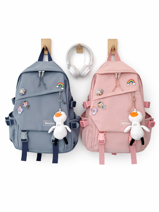 白背景に、グレーがかったブルーと淡いピンクのリュックが2点、正面向きで並んでいる。両方ともレインボーなどのピンバッジと、白いアヒルのぬいぐるみチャームが付いており、上部にフックで掛けられている。下に柔らかな影が入っている。
