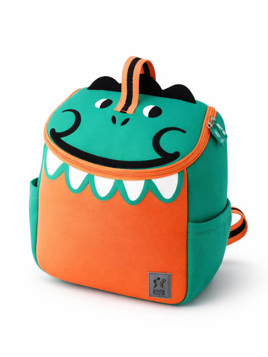 白背景に、ターコイズとオレンジ配色の恐竜モチーフの子ども用リュックが斜め前向きに写っている。フタ部分に目と鼻のデザインがあり、口元は白い歯の形の縁取り。上部にオレンジ×黒の持ち手が付いており、下に自然な薄い影が入っている。
