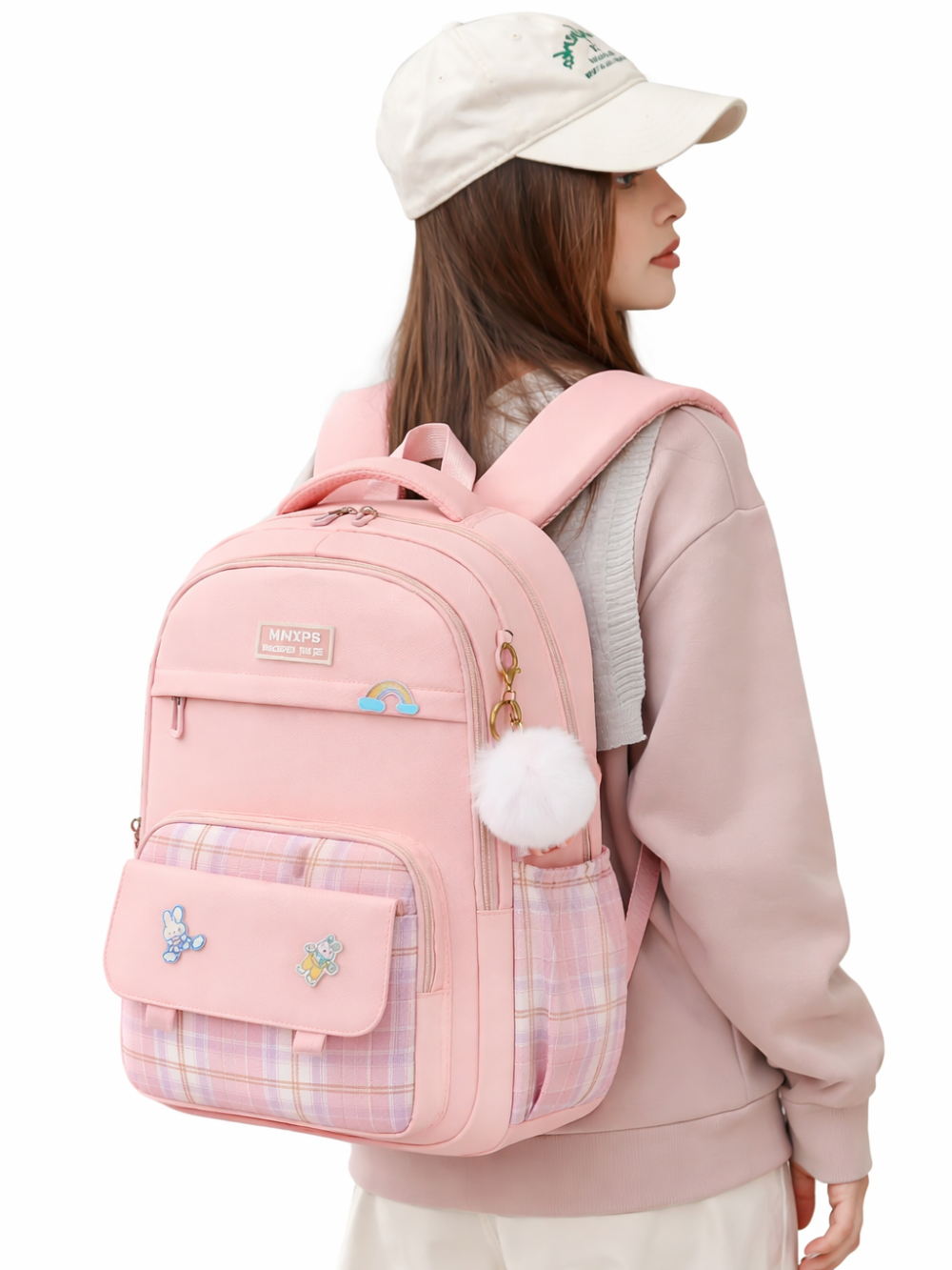 白背景で、ベージュのキャップをかぶった女性が、チェック柄ポケットと白いポンポンチャーム付きの淡いピンクのリュックを背負って横向きに立っている。