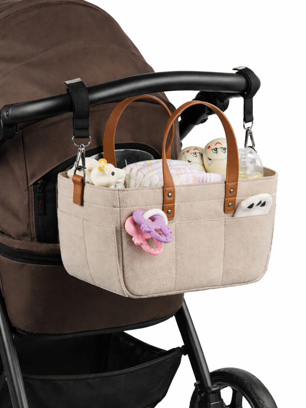 ベージュのキャンバス地ベビーカーバッグ（ストローラーオーガナイザー）が黒いベビーカーのハンドルに取り付けられ、哺乳びんやおむつなどの小物を入れている様子。
