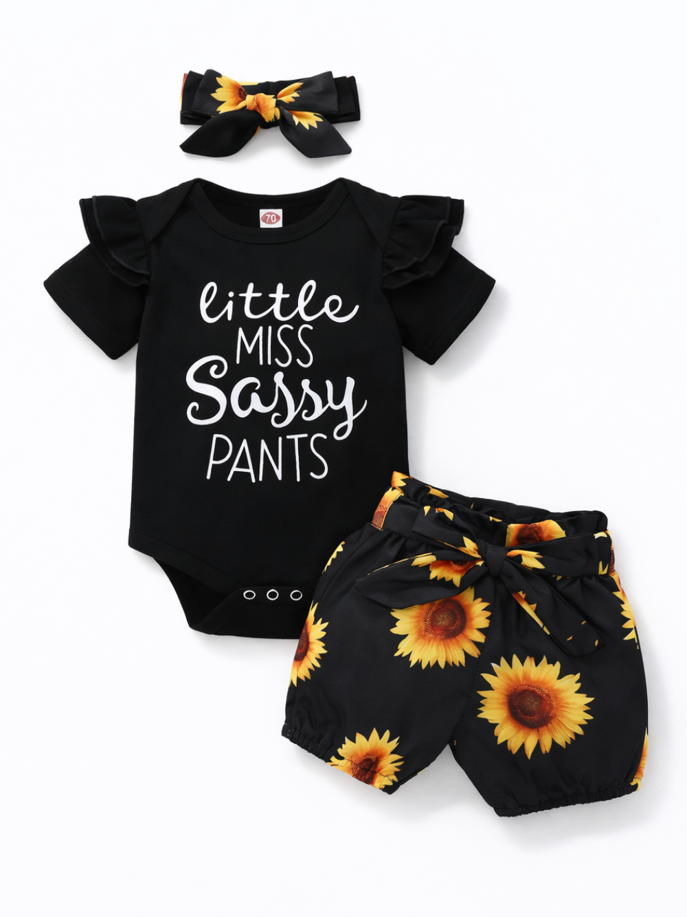 黒の半袖ベビー用ロンパース（胸に「little MISS SASSY PANTS」のプリント、肩にフリル）と、ひまわり柄のショートパンツ、同柄のリボンヘアバンドの3点セットを、白い背景に並べた商品画像。