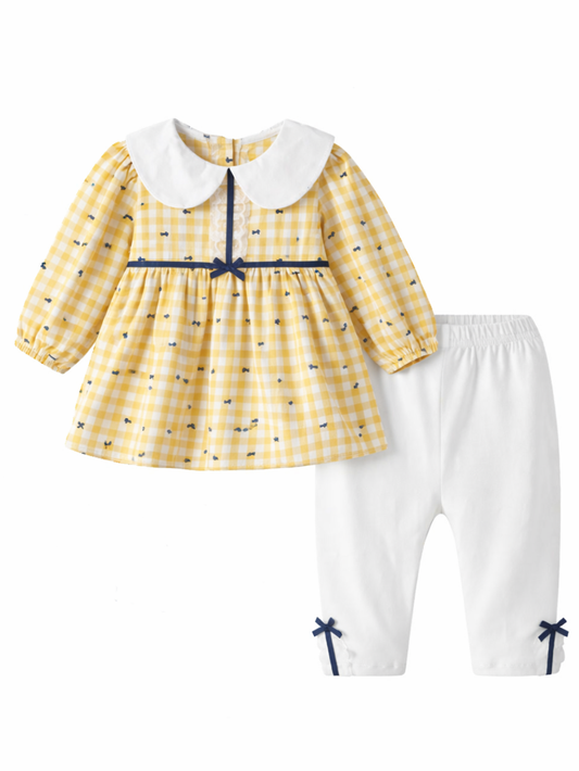 黄色のギンガムチェック柄ワンピース風トップスと白いパンツの2点セット。大きめの白い襟とネイビーのリボン、ふんわり長袖が特徴で、パンツ裾にも小さなリボンが付いている。