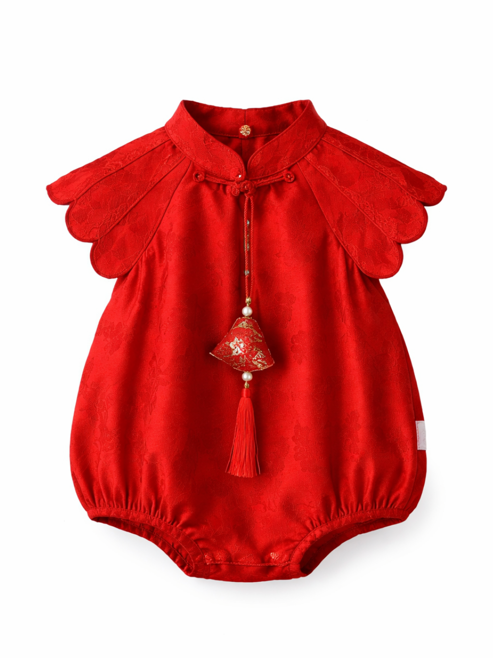 赤いチャイナ風のベビーロンパース。立ち襟と貝殻形の肩フリル付きで、胸元に飾り結びと鈴・房飾りが下がり、白背景に単体で撮影されている。
