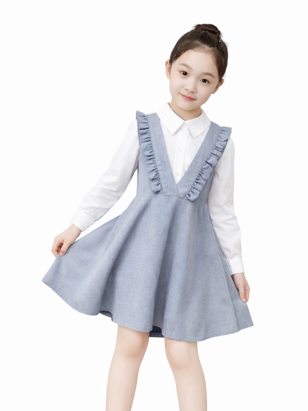 白背景に、グレーのジャンパースカート（フリル付きVネック）を白い襟付きシャツの上に着た女の子が立っている。片手でスカートの端をつまみ、黒いフラットシューズを履いている。
