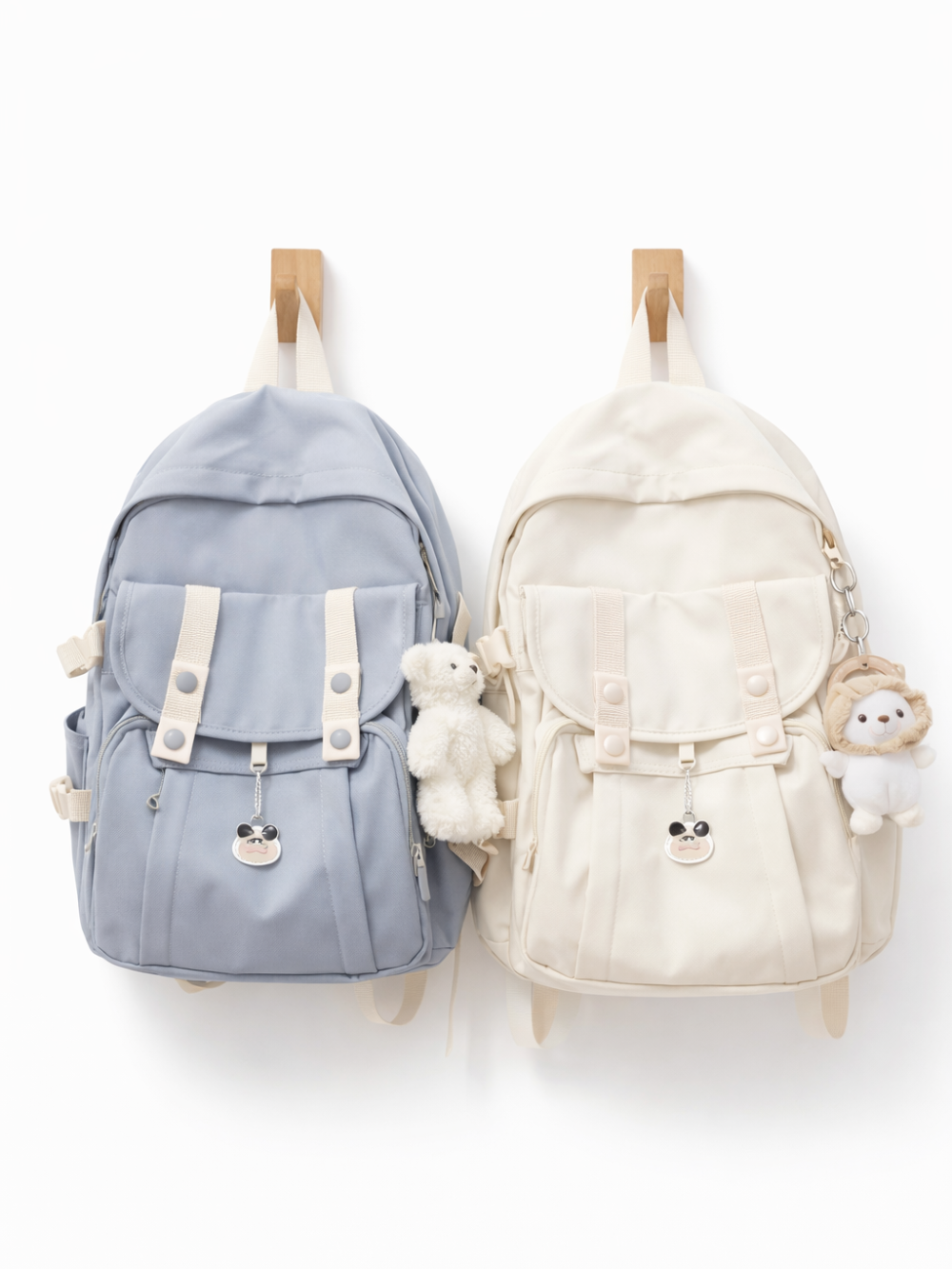 白背景に、木製フックに掛かったリュックが2つ並んでいる。左はライトブルー、右はアイボリーで、前面フラップとベルト留めのポケット、サイドポケット付き。ぬいぐるみチャームと小さなキャラクターチャームが付いている。
