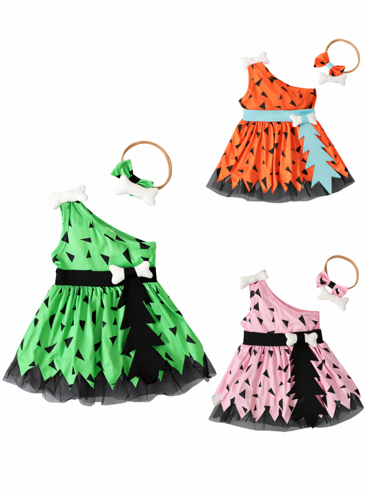 白背景に配置された、ワンショルダーのキッズドレス3点セット。グリーン／オレンジ／ピンクの三角柄で、黒いチュールの裾とベルト風デザイン付き。骨モチーフのヘアアクセサリー（カチューシャ）も写っている。
