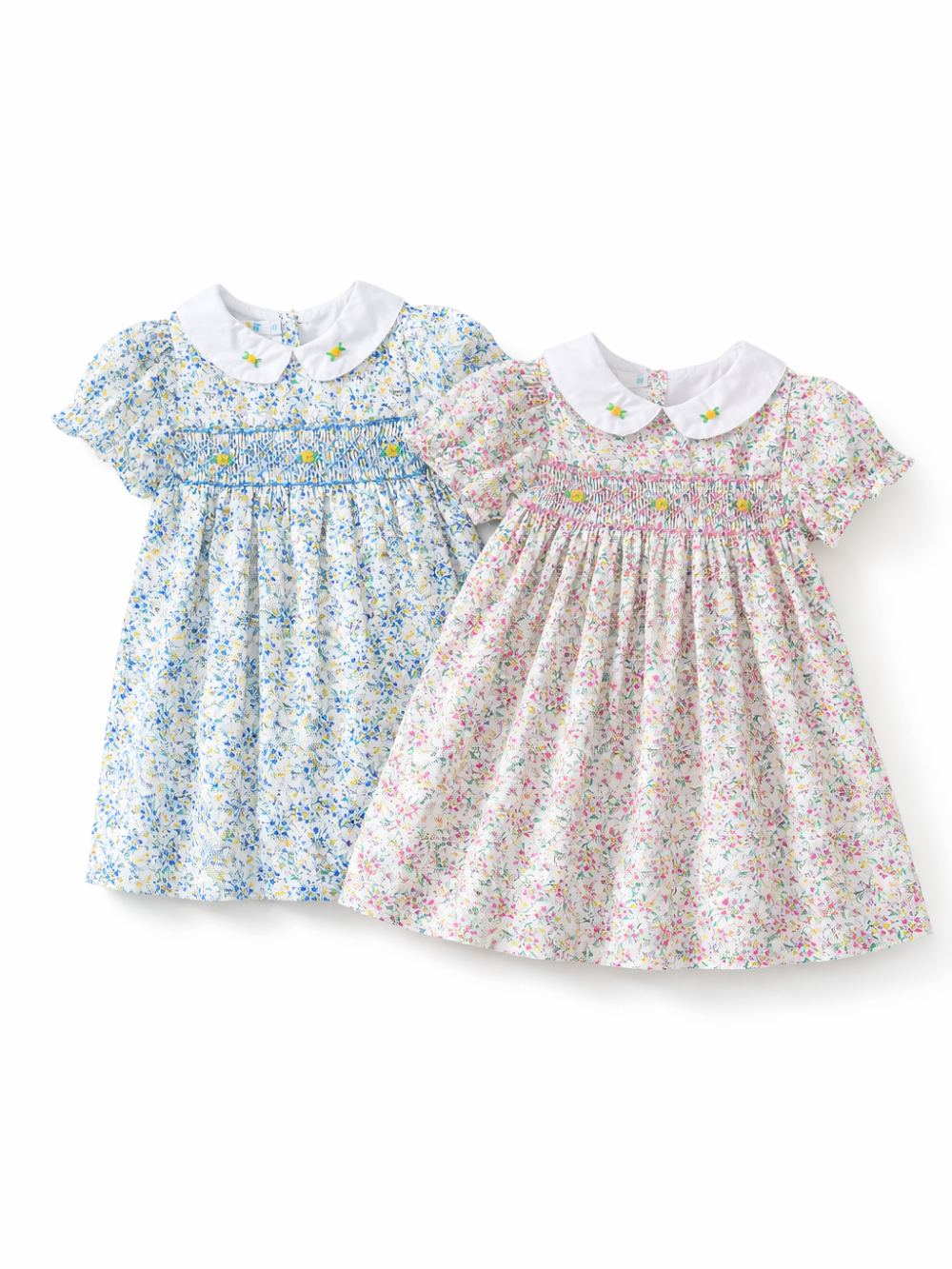 白背景に並べられたキッズワンピース2点。どちらも白い丸襟に小さな花刺繍があり、胸元はシャーリング仕様。左はブルー系の小花柄、右はピンク系の小花柄で、ふんわり広がるシルエット。
