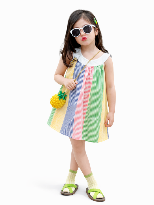 白背景のスタジオで、白いサングラスと緑のヘアピンを付けた女の子が、カラフルな縦ストライプのノースリーブワンピースを着て、パイナップル形のミニバッグと黄緑のサンダルを合わせてカタログ風にポーズを取っている。
