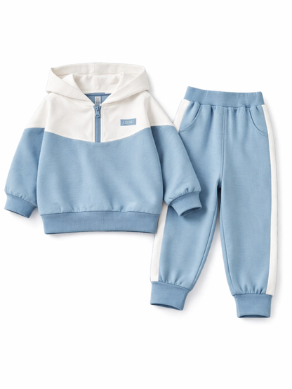 白い背景に、子ども用のツートンカラーのフーディーとジョガーパンツの2点セットがフラットレイで配置されている。フーディーはホワイト×ライトブルーでハーフジップ仕様、パンツはライトブルーでサイドにホワイトラインが入り、ウエストと裾はリブになっている。

