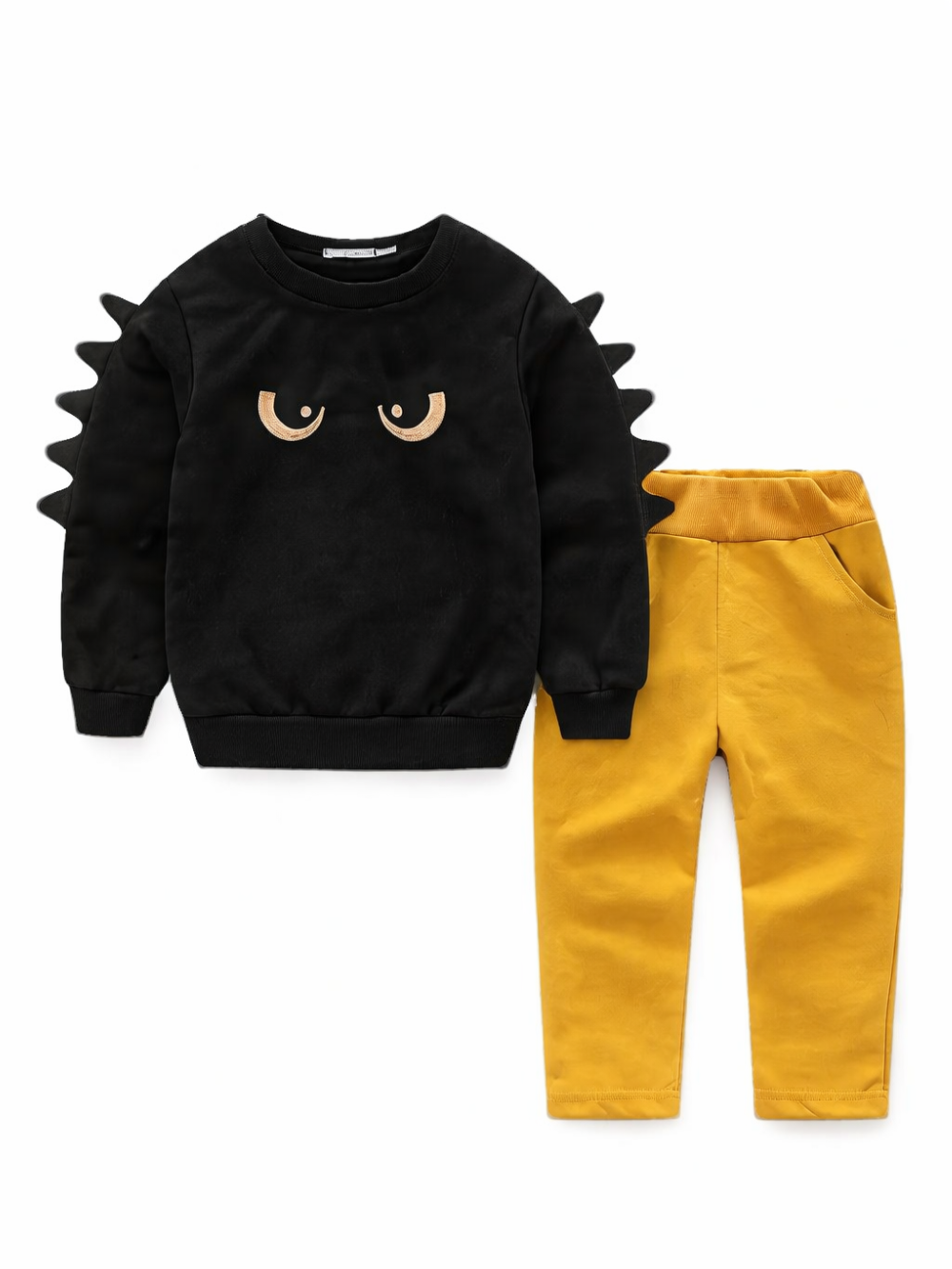 白い背景に、子ども用の上下セットがフラットレイで配置されている。トップスはブラックの長袖スウェットで胸元に目の刺繍があり、袖の外側にトゲ状の立体ディテールが付いている。ボトムスはマスタードカラーのロングパンツで、ウエストはリブ仕様、サイドポケット付き。
