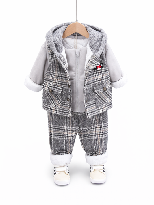 白い背景に、フード付きチェック柄ベストとグレーのジップトップス、チェック柄パンツを合わせた幼児用コーディネートがハンガーに掛けて展示されている。袖口と裾は白いボア風の縁取りで、足元にはクリーム色のスニーカーが写っている。
