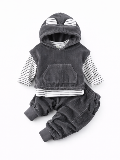 白い背景に、ダークグレーのコーデュロイ素材フード付きトップスと同素材のパンツを合わせた子ども用セットがフラットレイで配置されている。フードにはボーダー柄の耳モチーフが付き、インナーとして白×黒ボーダーの長袖トップスが重ねられている。トップス前面にカンガルーポケットがある。
