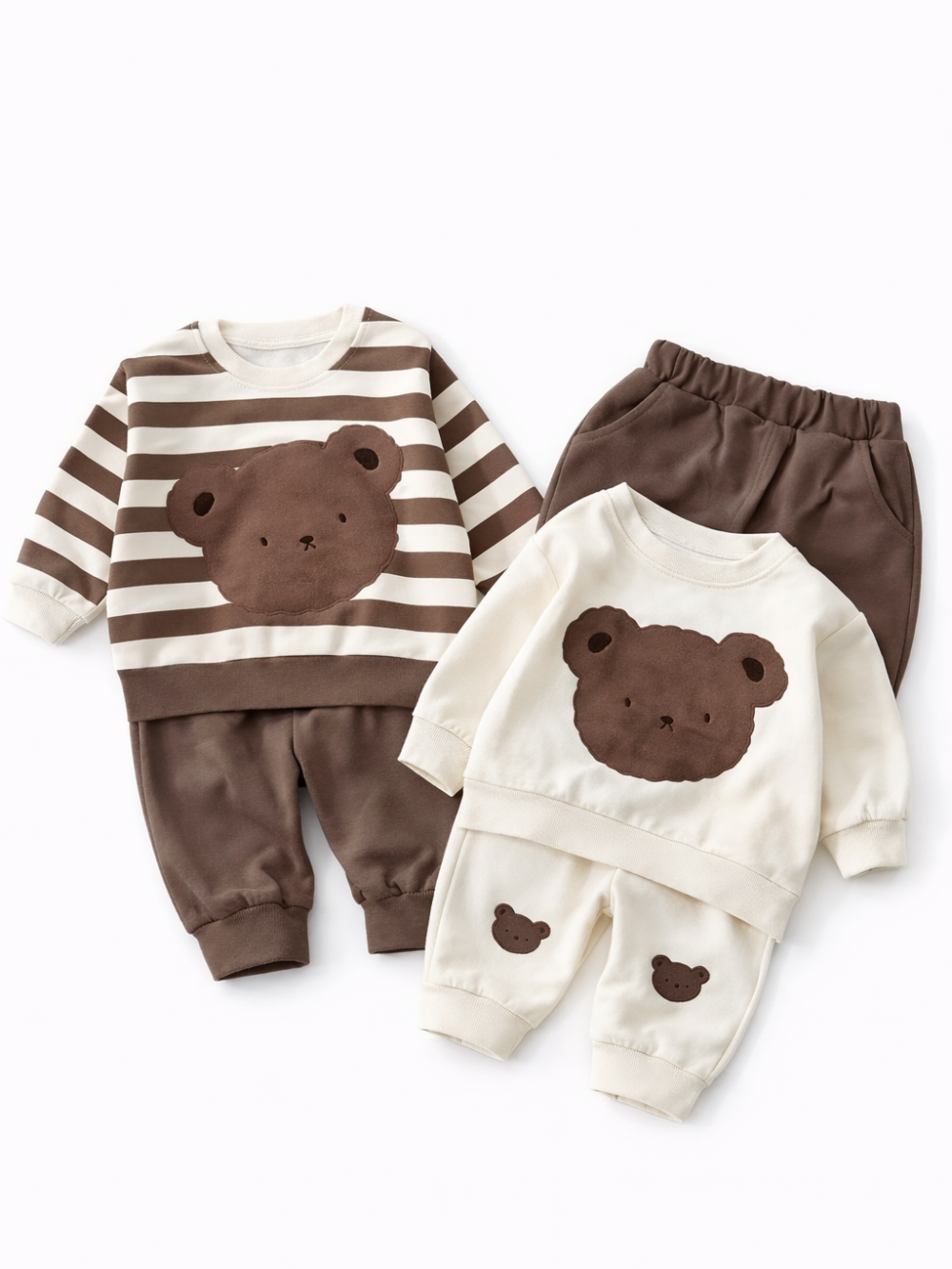 白い背景に、クマのモチーフが付いた子ども用セットアップが2組並べて配置されている。1組はブラウン×アイボリーのボーダー長袖トップスとブラウンのパンツ、もう1組はアイボリーの長袖トップスとパンツで、トップスにクマの顔アップリケ、パンツの脚部分に小さなクマのモチーフが付いている。
