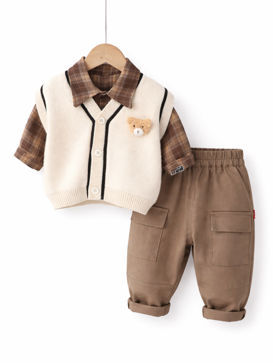 白い背景に、幼児用のチェック柄シャツ、ニットベスト、カーゴパンツの3点コーディネートがハンガーに掛けて展示されている。ブラウン系チェックの半袖シャツの上にアイボリーのVネックベストを重ね、胸元にクマのワッペンが付いている。ボトムスはブラウンのウエストゴムカーゴパンツで、大きなポケットが付いている。
