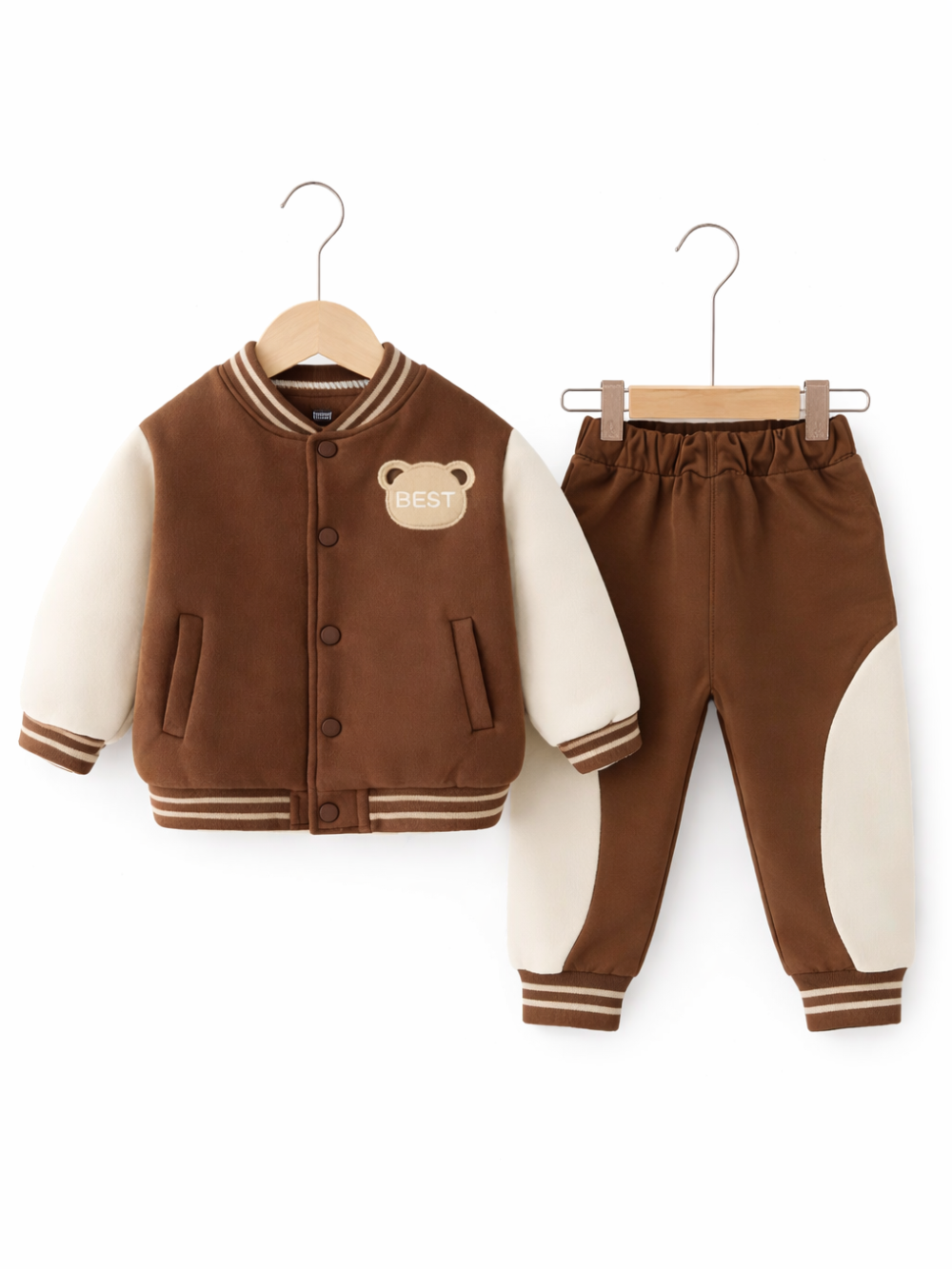 白い背景に、子ども用のジャケットとパンツの上下セットがハンガーに掛けられて並んでいる。ジャケットはブラウン×アイボリーの切り替えでスナップボタン留め、胸元にクマ型の「BEST」ワッペンが付いている。パンツはブラウンでサイドにアイボリーの切り替えがあり、裾はリブ仕様になっている。
