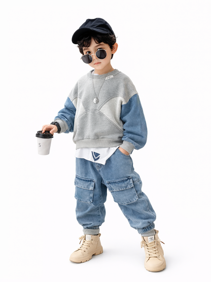 白い背景に、キャップとサングラスを着用した男の子が立っている。グレー×デニムブルーの切り替えスウェットとデニムのカーゴパンツを着て、ベージュのブーツを履いている。片手に紙コップを持ち、もう片方の手はポケットに入れ、首元にペンダントネックレスと腕時計を付けている。
