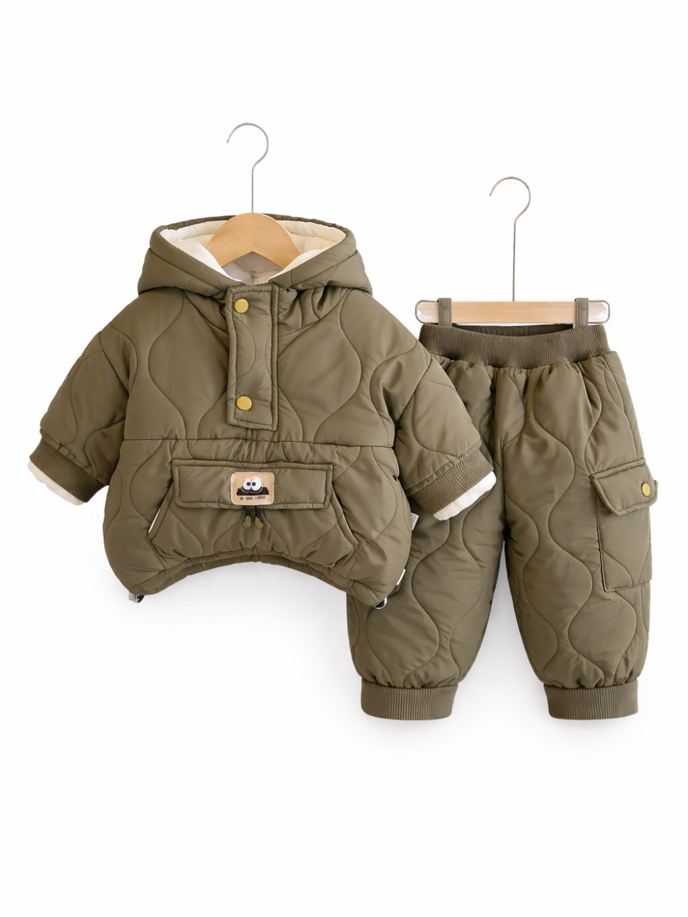 白い背景に、オリーブグリーンのキルティング素材の子ども用中綿ジャケットとパンツの上下セットがハンガーに掛けられて並んでいる。ジャケットはフード付きでスナップボタン留め、前面にフラップ付きポケットと小さなワッペンがある。パンツはウエストゴムで、サイドポケットと裾リブ仕様になっている。
