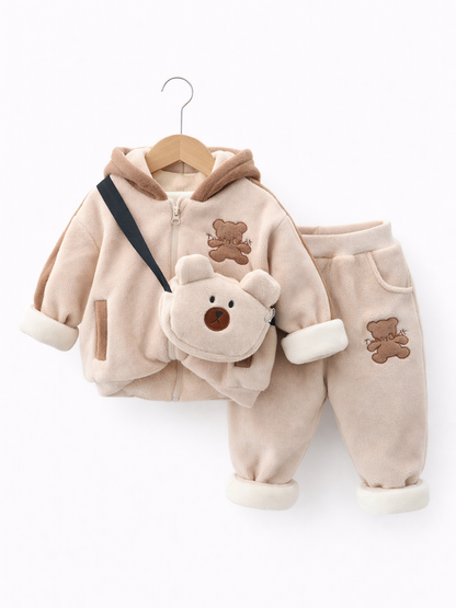 ベージュのもこもこ素材のベビー上下セット（フード付きジップジャケット＋パンツ）。クマのワッペンとクマ型ショルダーバッグ付きで、木製ハンガーに掛けられた状態を白背景で撮影している。

