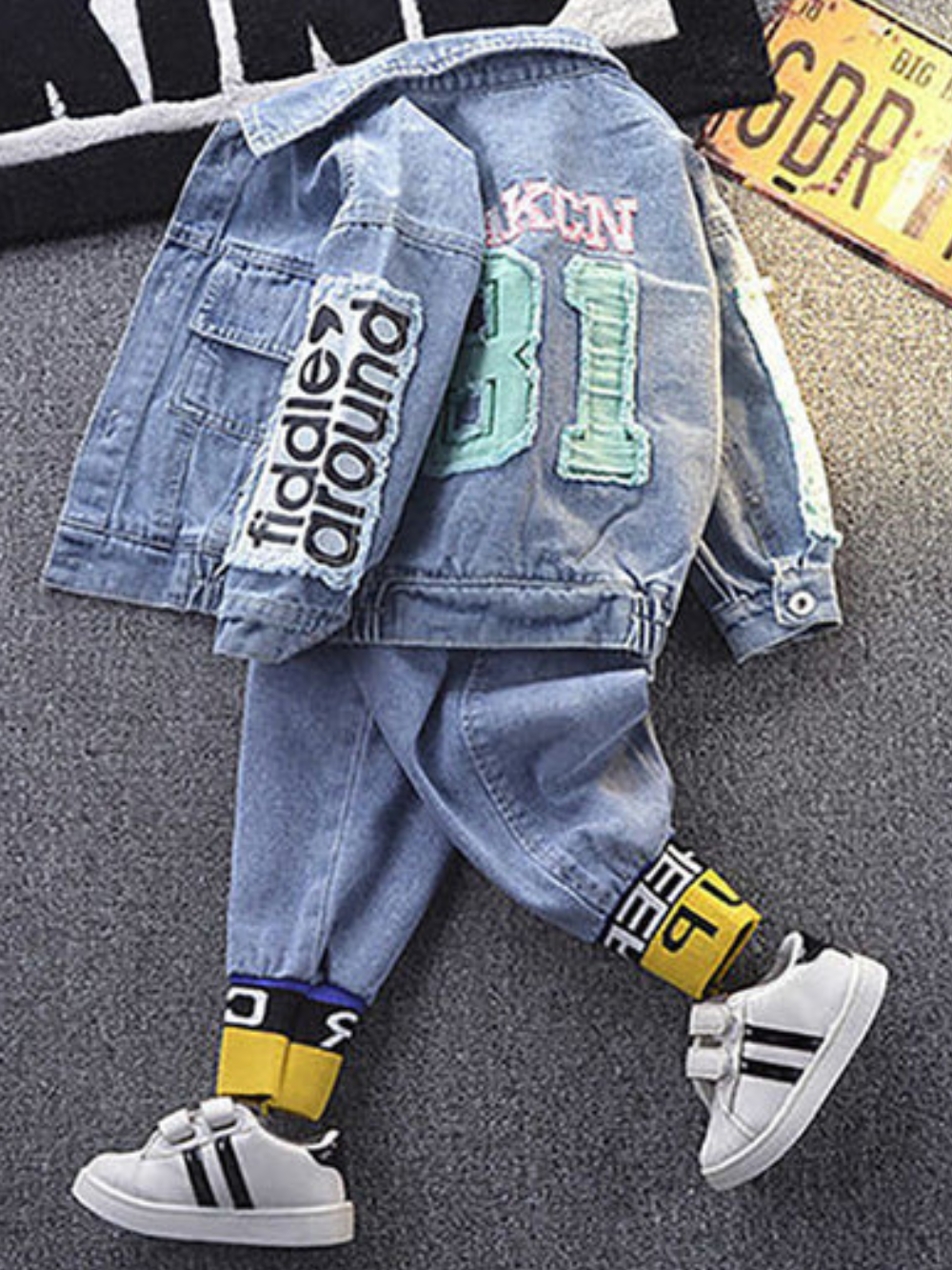 床に並べられた子ども用デニムジャケットとデニムパンツのセット。背中に「31」のワッペン、袖にロゴパッチが付いており、黄色×黒のソックスと白いベルクロスニーカーを合わせている。
