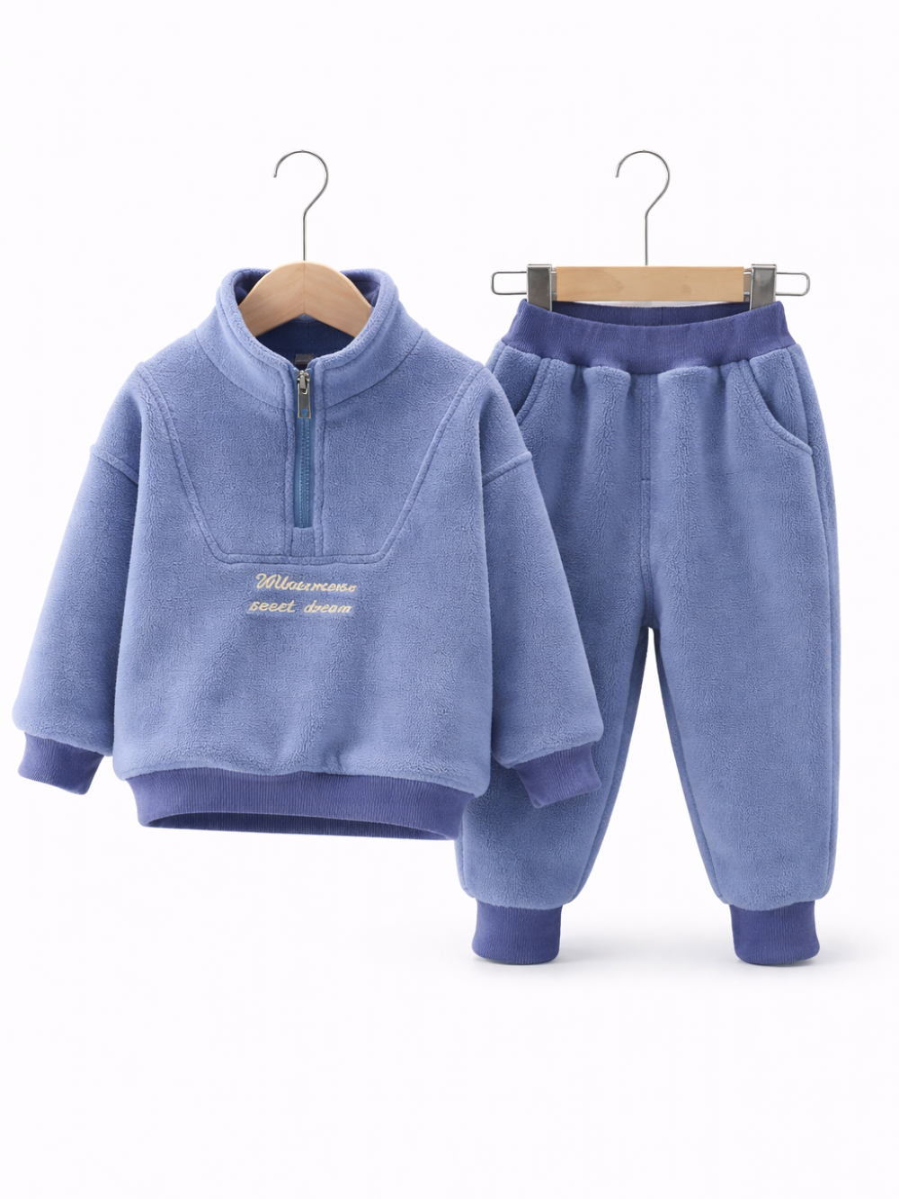 ライトブルーのフリース素材の子ども用上下セット（ハーフジップのトップスとジョガーパンツ）が、白背景のスタジオでハンガーに掛けて並べて展示されている。
