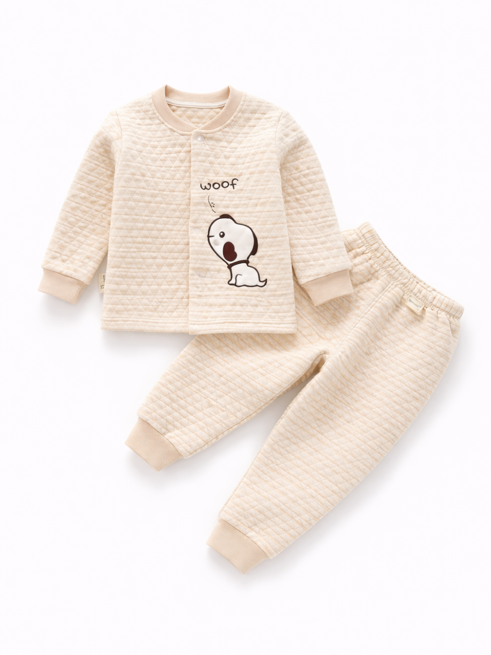 生成り色のキルティング生地のベビー用上下セット（長袖トップスとパンツ）。トップスに「woof」と犬のイラストがあり、白背景に平置きで撮影されている。
