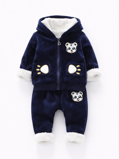 ネイビーのベロア調フード付きジップパーカーと、同素材のパンツのベビー用上下セット。フード内側と袖口・裾に白いボアが付き、胸とパンツに動物の顔ワッペン、ポケットに肉球モチーフの刺繍がある。白背景で正面から整えて撮影された商品画像。
