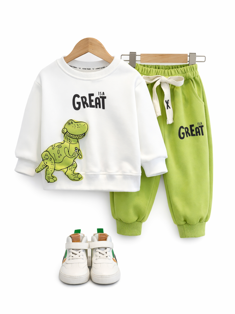白いスウェット（恐竜イラストと「GREAT」ロゴ）とライムグリーンのジョガーパンツ、白いスニーカーをハンガーに掛けて並べた子ども用セットアップ。背景は純白。
