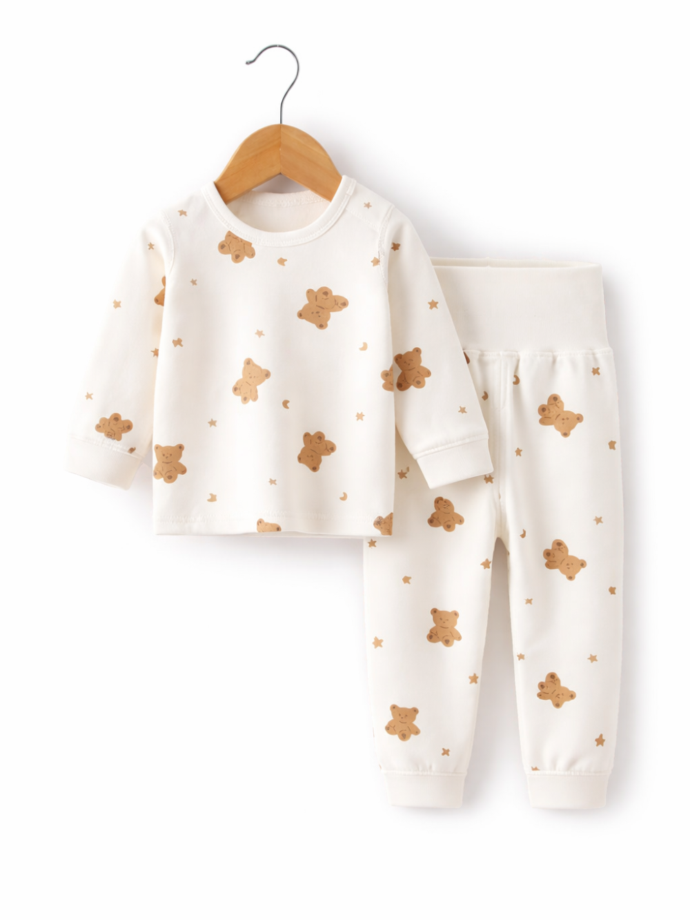 オフホワイトのベビー用上下セット。くま・星・三日月の総柄プリントの長袖トップスが木製ハンガーに掛かり、同柄のロングパンツが横に並んだ白背景のスタジオ撮影。
