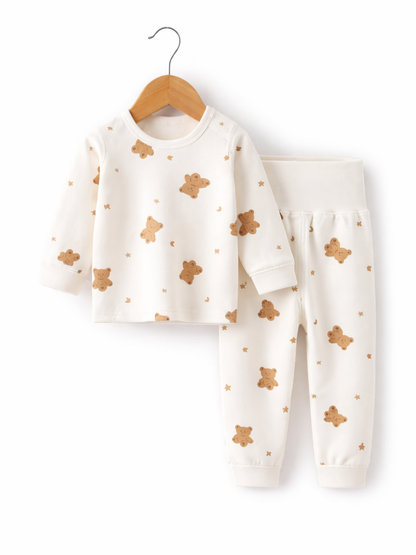 オフホワイトのベビー用上下セット。くま・星・三日月の総柄プリントの長袖トップスが木製ハンガーに掛かり、同柄のロングパンツが横に並んだ白背景のスタジオ撮影。
