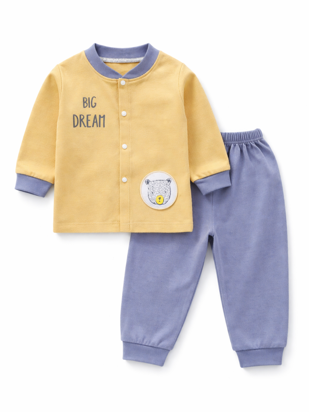 白背景のスタジオ風に、キッズ用ルームウェア上下セットが並べて撮影されている。マスタードイエローの前開きトップスは「BIG DREAM」プリントとクマのワッペン付きで、襟・袖口はブルー。合わせたブルーのロングパンツはウエストゴムと裾リブ仕様。
