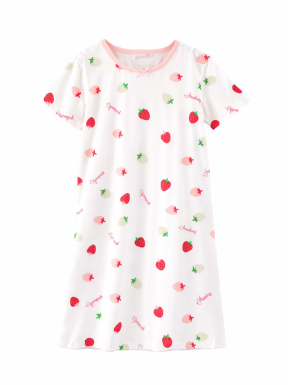 白い半袖のキッズ用ワンピース（ナイトドレス）が白背景で平置きされている。ピンクの襟ぐりと小さなリボンがあり、いちごやピーチの柄と「Strawberry」の文字が散りばめられている。
