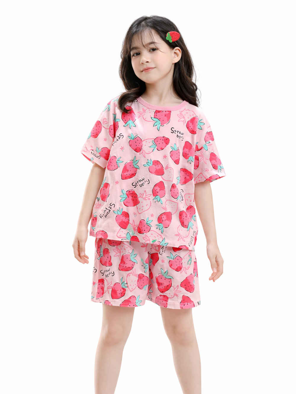白背景のスタジオで、いちご柄のピンクの半袖トップスとショートパンツを着た女の子が、自然なモデルポーズで立っている写真。
