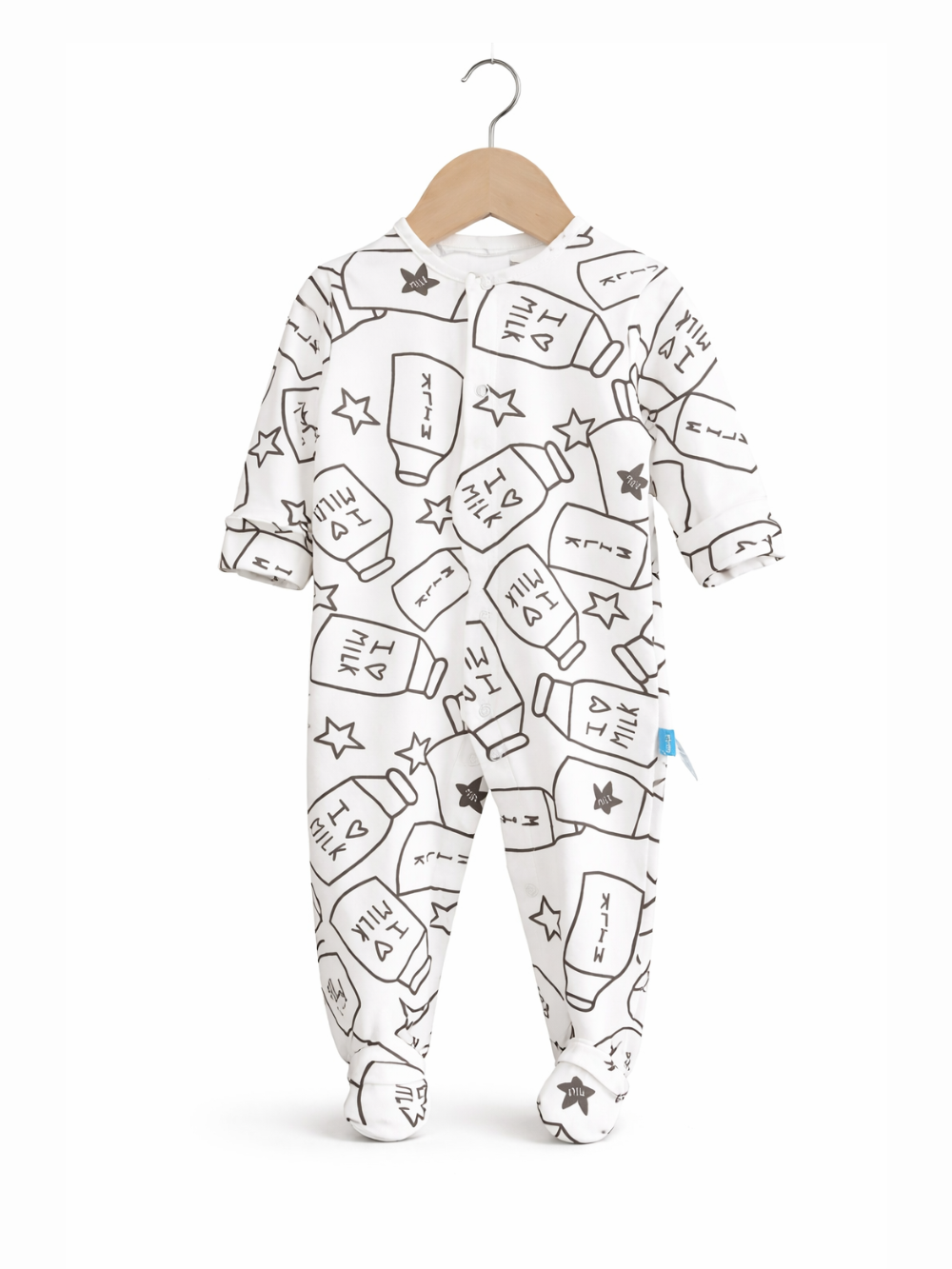 白背景に、木製ハンガーに掛けられた白いベビー用足つきロンパース（ミルクボトルと星の黒い総柄プリント）が写っている商品写真。
