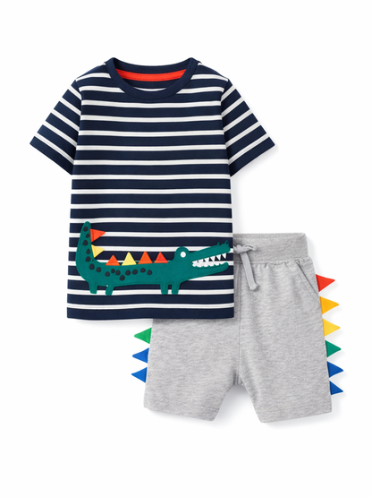 白背景のスタジオ撮影で、子ども用2点セットを正面から配置。ネイビー×白ボーダーの半袖Tシャツにワニのアップリケ、グレーのショートパンツはサイドにカラフルなスパイク装飾付き。
